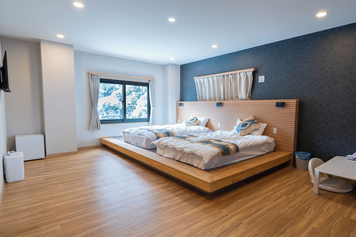 Quarto moderno com uma cama grande, uma mesinha e uma janela com cortinas.