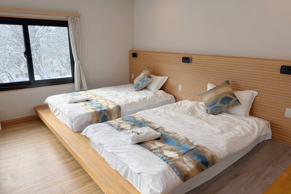 Quarto com duas camas, cabeceira de madeira, janela com vista para árvores cobertas de neve e piso em tons claros.