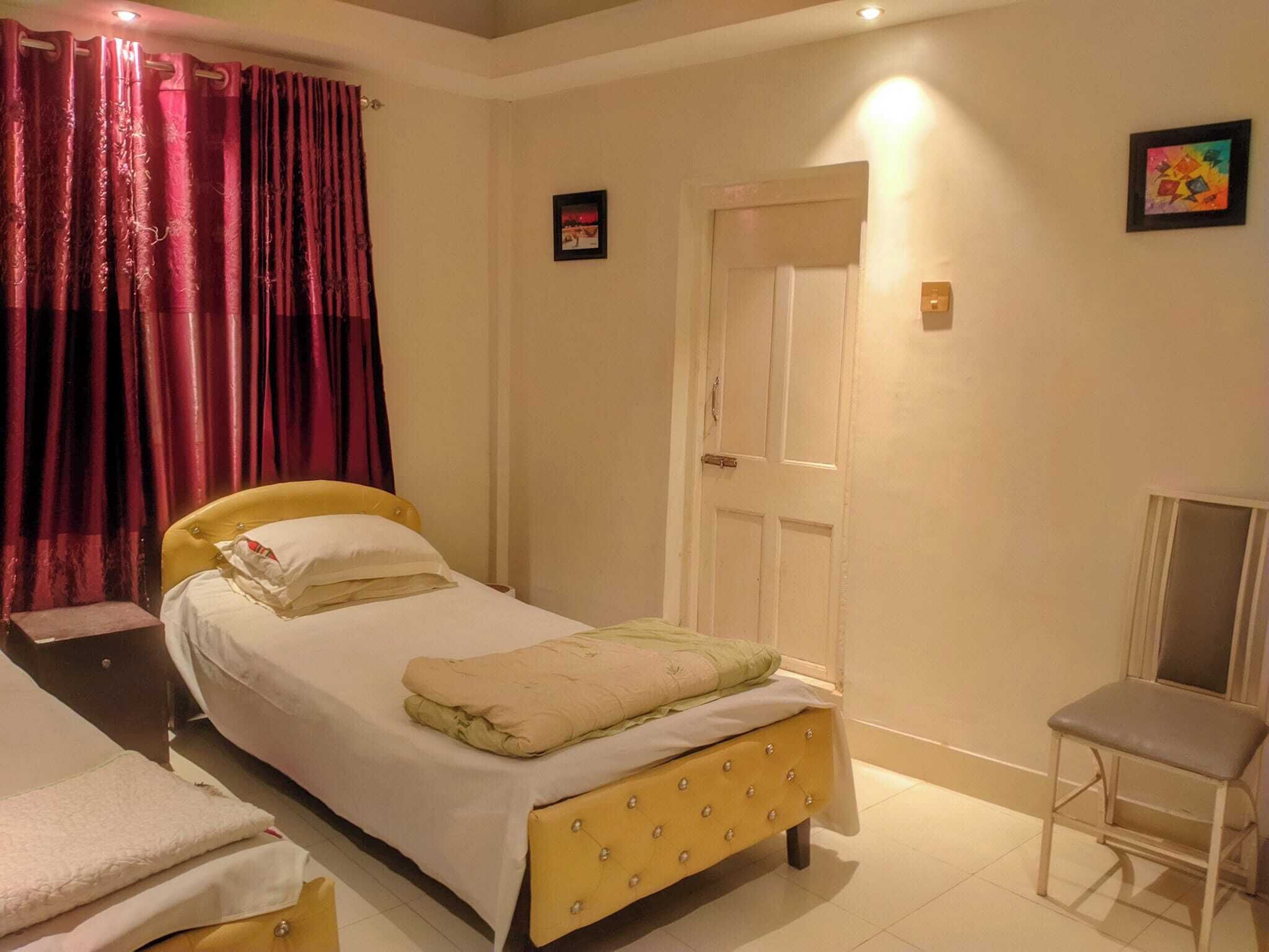 Een slaapkamer met een bed, een stoel, een deur en gordijnen.