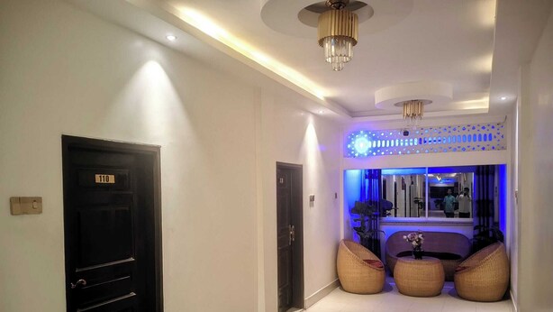 A hallway with a black door labeled '110', a reception area with a blue-lit window, and wicker seating. - Gazi Residential Hotel Chandpur (Chandpur)