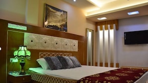 A hotel room with a bed, a nightstand with a lamp, a television, and a painting on the wall. - Gazi Residential Hotel Chandpur (Chandpur)