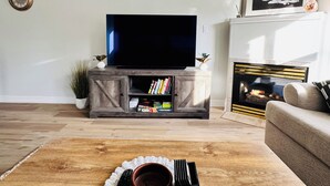 Ein Wohnzimmer mit Flachbildfernseher auf einer Holzkommode, Kamin und einer Couch.