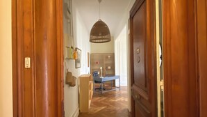 A wooden door leading to a hallway with a desk and chair, a hanging light fixture, and a view into a room with a bed and a window. - Bourgeois apartment 2 min from Bellecour. (Lyon)