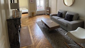 A living room with a herringbone wooden floor, a grey sofa, a round mirror, and a wooden coffee table. - Bourgeois apartment 2 min from Bellecour. (Lyon)