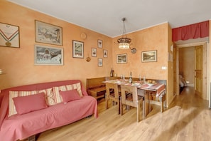 A cozy living room with a wooden dining table set for four, a red sofa, and various framed pictures on the walls. - Rochebrune 5th - Flat with Balcony for 4, Claviere, Italy (Claviere)