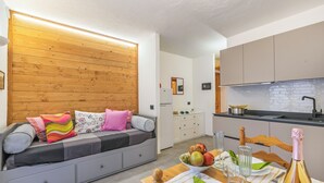 A modern kitchen with a wooden wall, a dining table with a bottle of champagne, and a fruit bowl. - Rochebrune 6th - Flat with Balcony for 4, Claviere, Italy (Claviere)