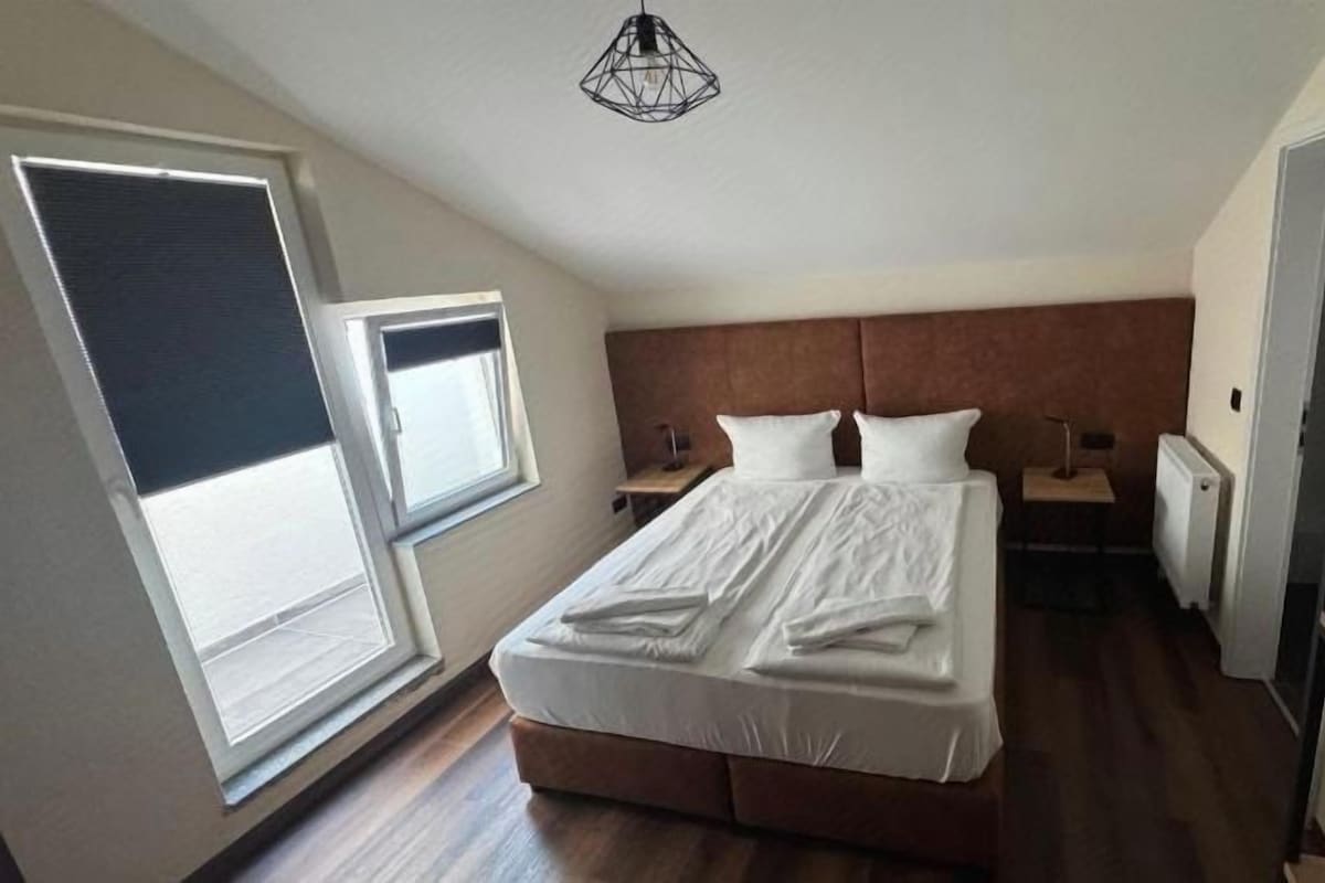 Ein Schlafzimmer mit Bett, Nachttischen, einem Fenster und einer Heizung.