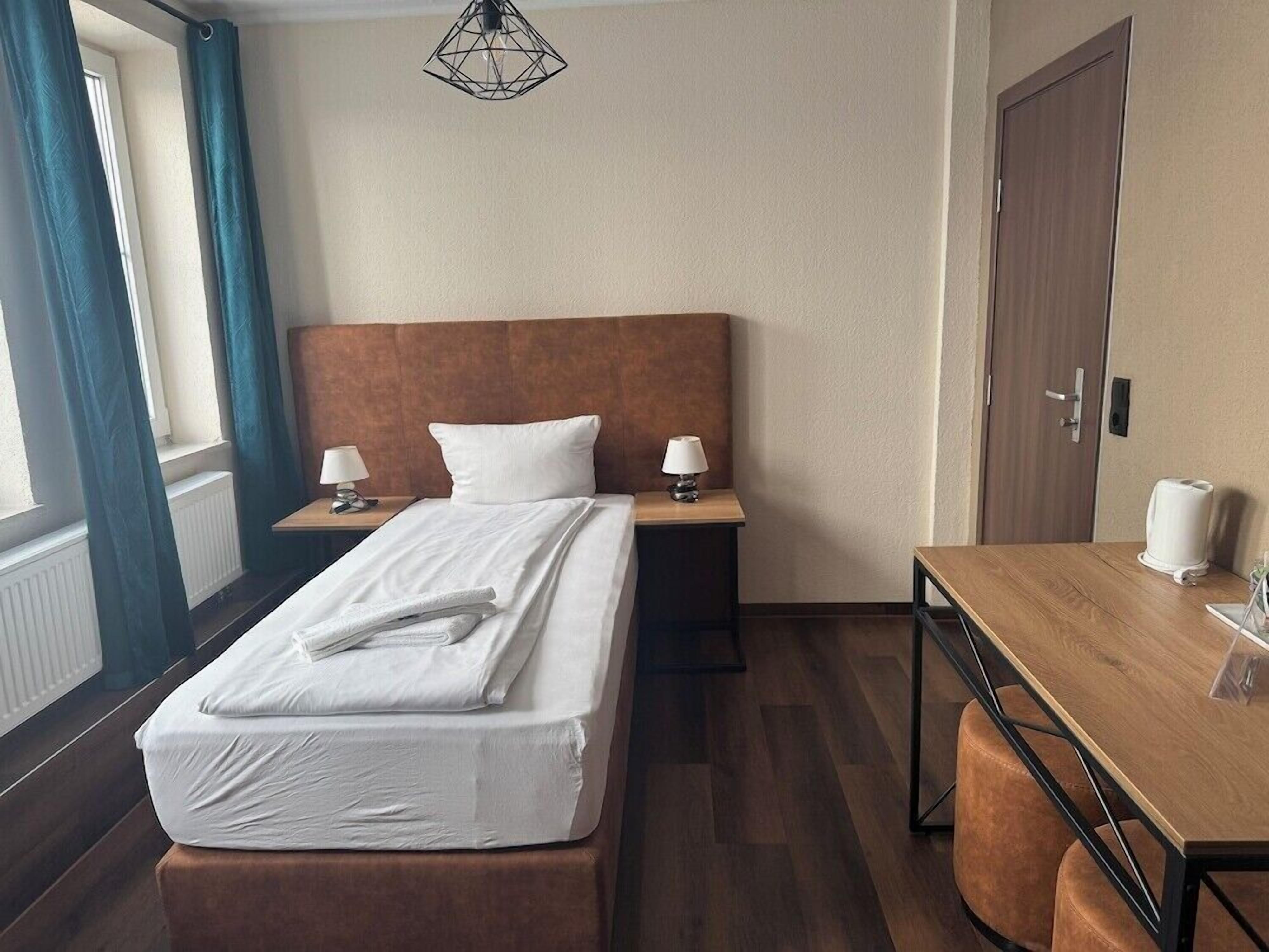 A hotel room with a bed, bedside tables, a desk, and a chair.