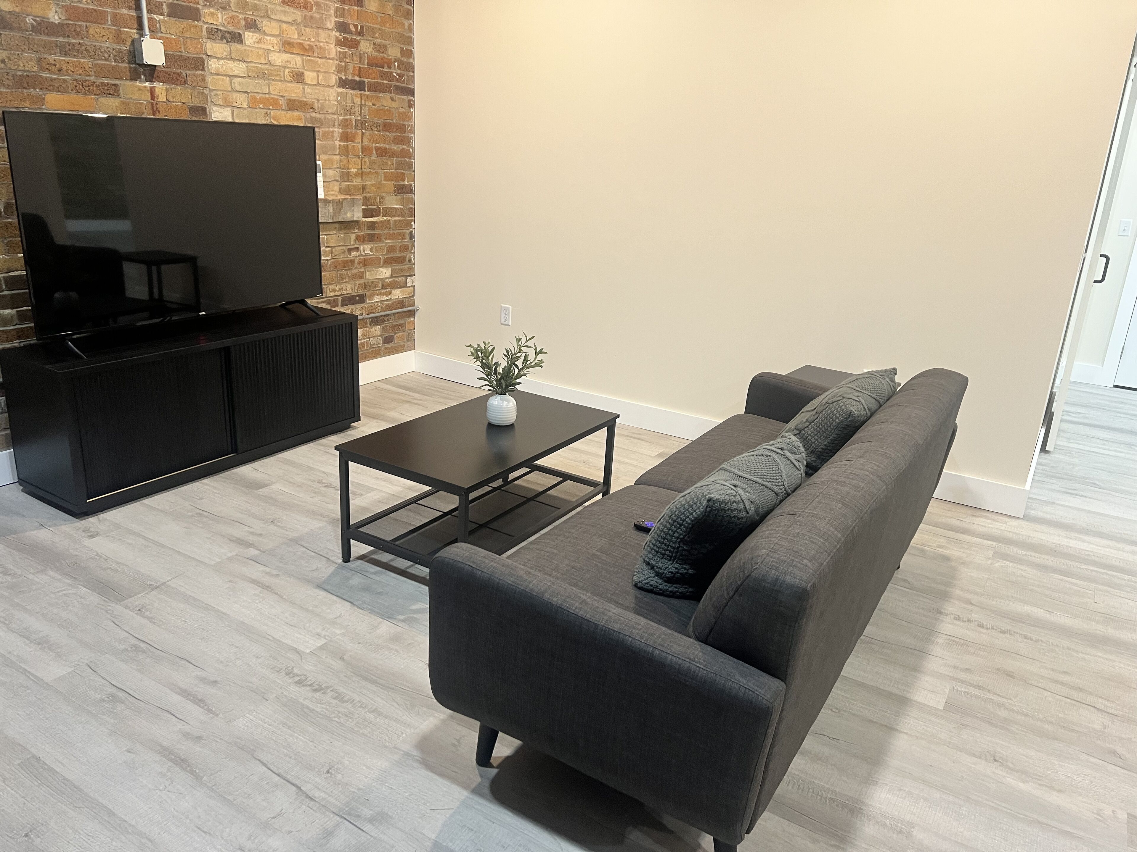 Una sala de estar moderna con televisor de pantalla plana, un sofá oscuro, una mesa de centro y una pared de ladrillo decorativa.