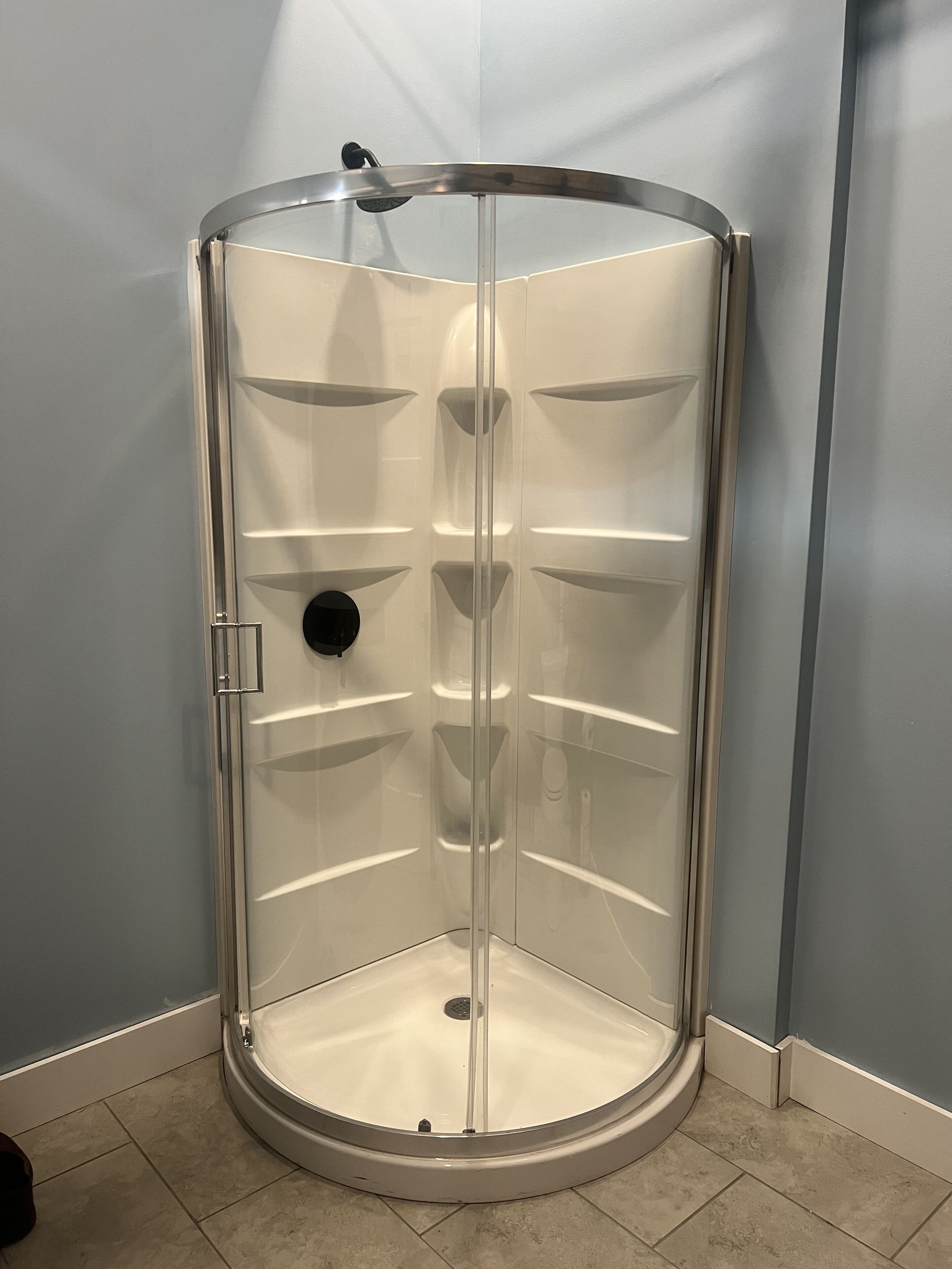A corner shower enclosure with a glass door and a metal frame.