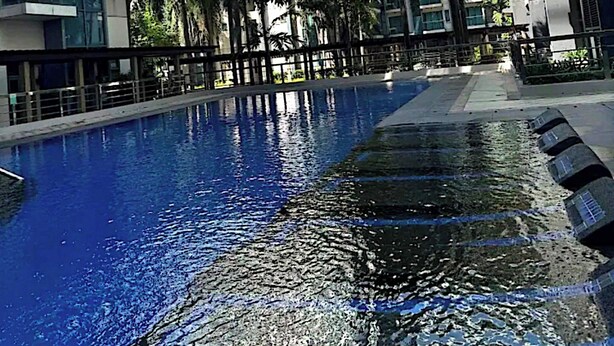 Un ensemble immobilier moderne comprenant un bâtiment principal et une piscine centrale, le tout entouré de palmiers et surplombé d’un ciel dégagé.