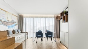 Una sala de estar moderna con sofá, mesa de comedor y sillas. Hay un cuadro en la pared y una ventana con cortinas.