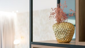 Un jarrón dorado con textura y flores secas rosas sobre un estante de madera.
