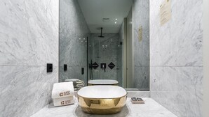 Un baño moderno con paredes de mármol, un lavamanos dorado redondo y cabina de ducha de vidrio.