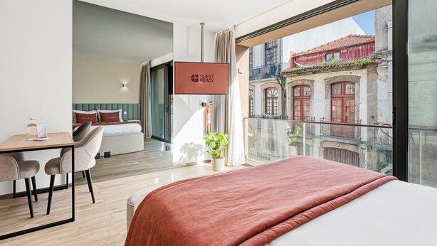 Camera d'albergo moderna con un letto grande, una scrivania e un balcone con vista su edifici storici.