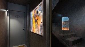 Un corridoio moderno con una porta grigia, un quadro astratto incorniciato e una scala che conduce a un balcone con vista sulla città.