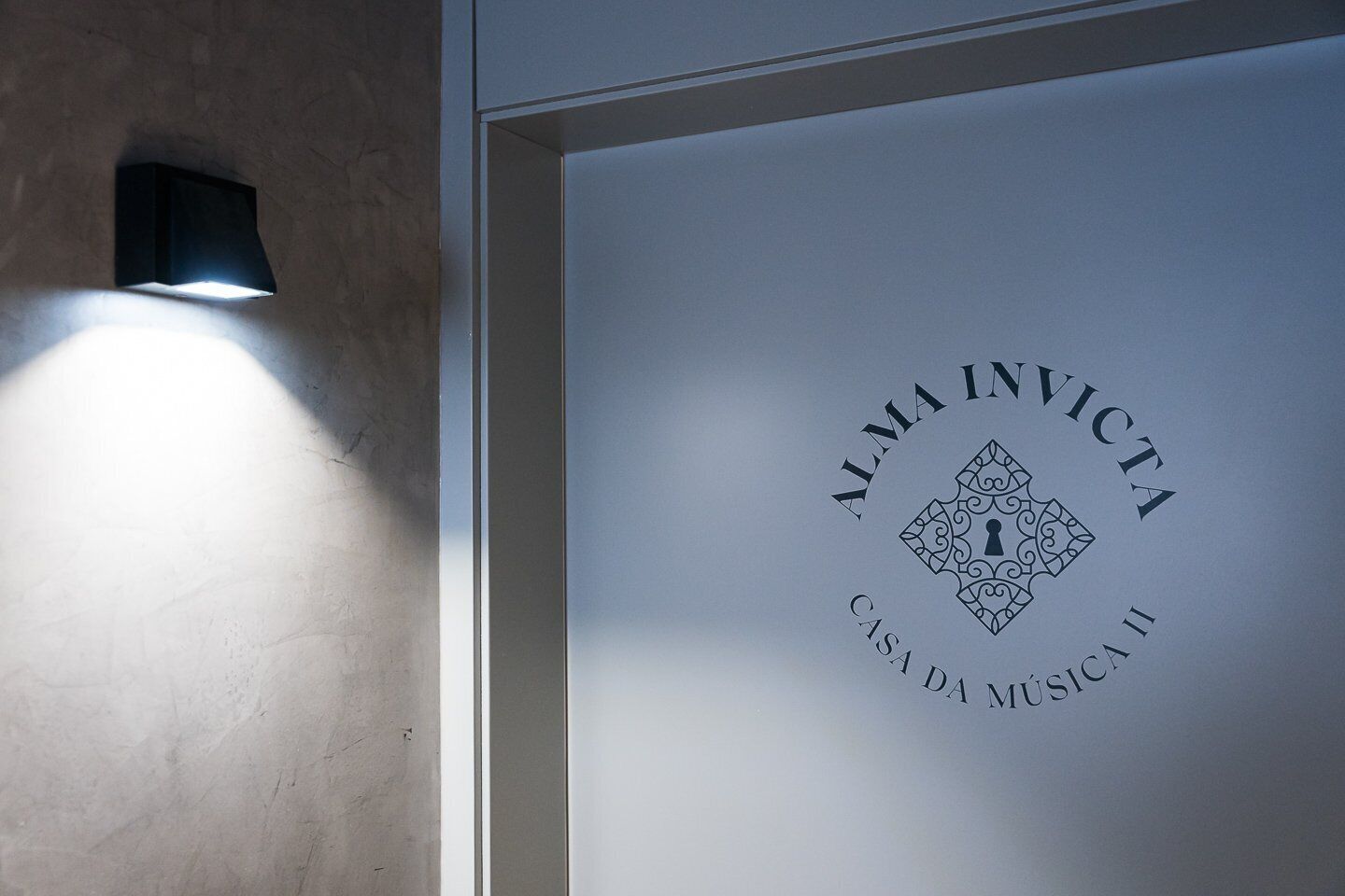 Eine Wand mit einer Leuchte und einem gerahmten Logo mit der Aufschrift 'ALMA INVICTA CASA DA MÚSICA'.