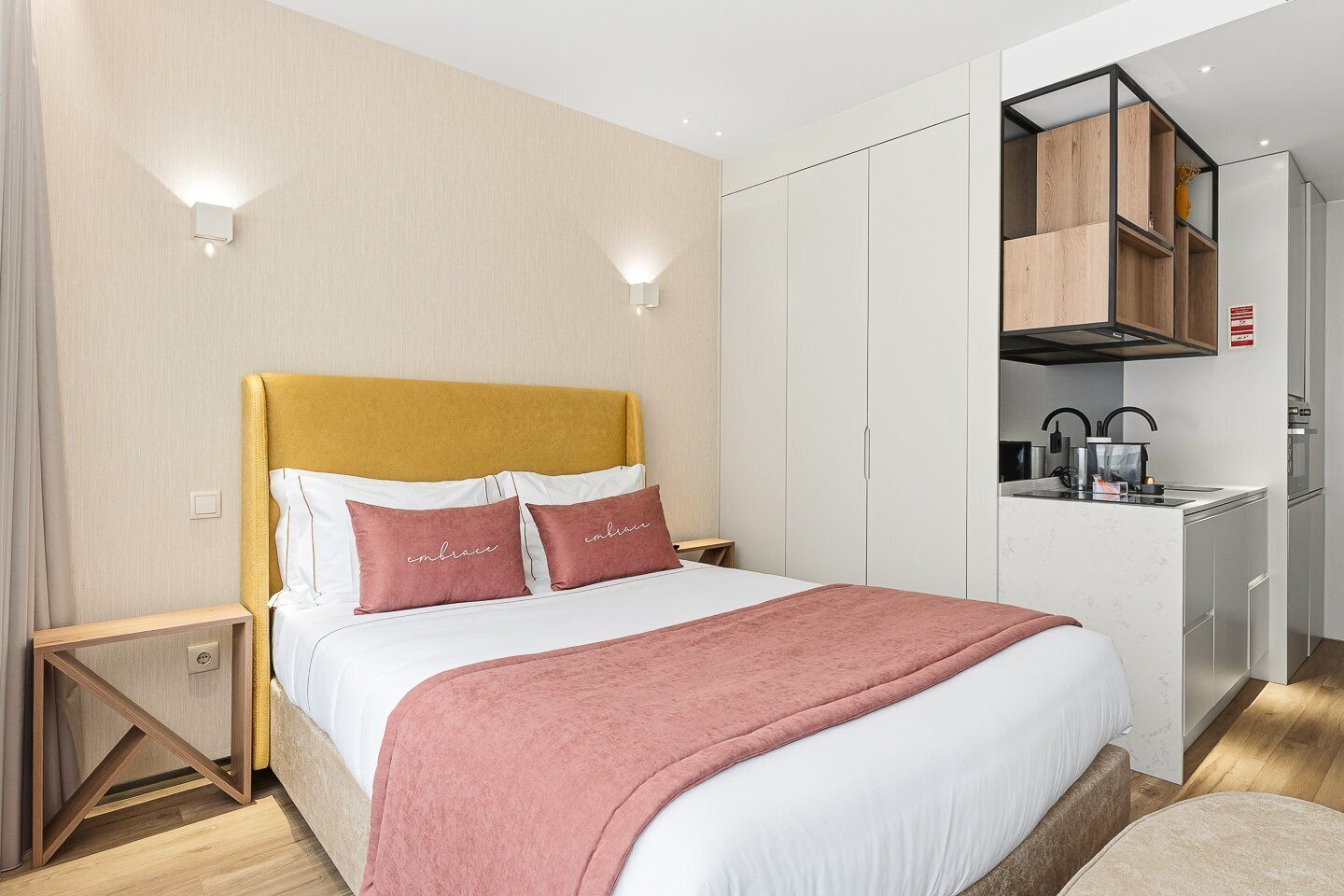 A modern bedroom with a bed, bedside tables, a wardrobe, and a kitchenette.