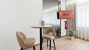 A modern hotel room with a round table, two chairs, a television, a fire extinguisher, and a potted plant. - GuestReady - Alma Invicta 'Casa da Música II' (Porto)