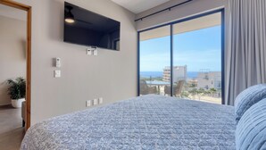 A bedroom with a large bed, a mounted TV, a sliding glass door to a balcony, and a potted plant. - 2-bedroom apartment in pleasant Cabo San Lucas with AC (Cabo San Lucas)