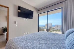 A bedroom with a large bed, a mounted TV, a sliding glass door to a balcony, and a potted plant. - 2-bedroom apartment in pleasant Cabo San Lucas with AC (Cabo San Lucas)