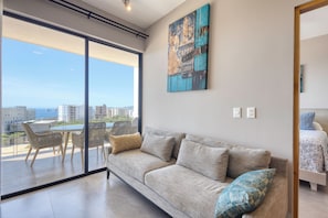 A modern living room with a large window, a sofa, and a dining area. - 2-bedroom apartment in pleasant Cabo San Lucas with AC (Cabo San Lucas)
