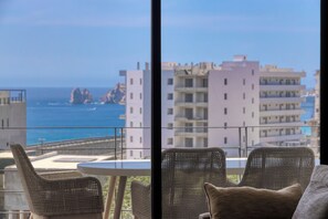 A balcony with wicker chairs and a table overlooking a coastal view with buildings and rocky formations. - 2-bedroom apartment in pleasant Cabo San Lucas with AC (Cabo San Lucas)