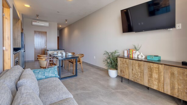 A modern living room with a sofa, dining table, and a TV mounted on the wall. - 2-bedroom apartment in pleasant Cabo San Lucas with AC (Cabo San Lucas)