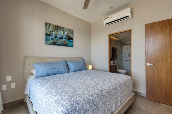 A bedroom with a bed, a painting, an air conditioner, and a wooden door. - 2-bedroom apartment in pleasant Cabo San Lucas with AC (Cabo San Lucas)