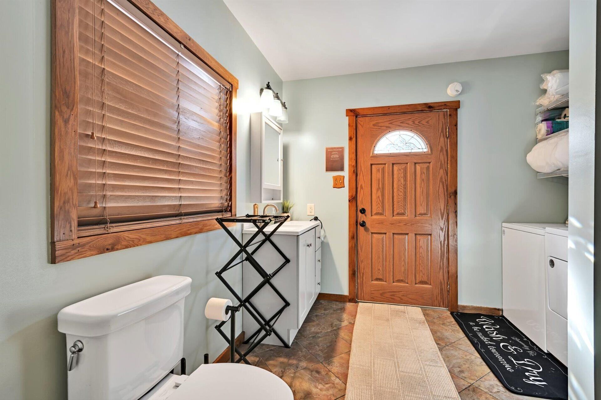 A bathroom with a toilet, a sink, a mirror, and a wooden door.