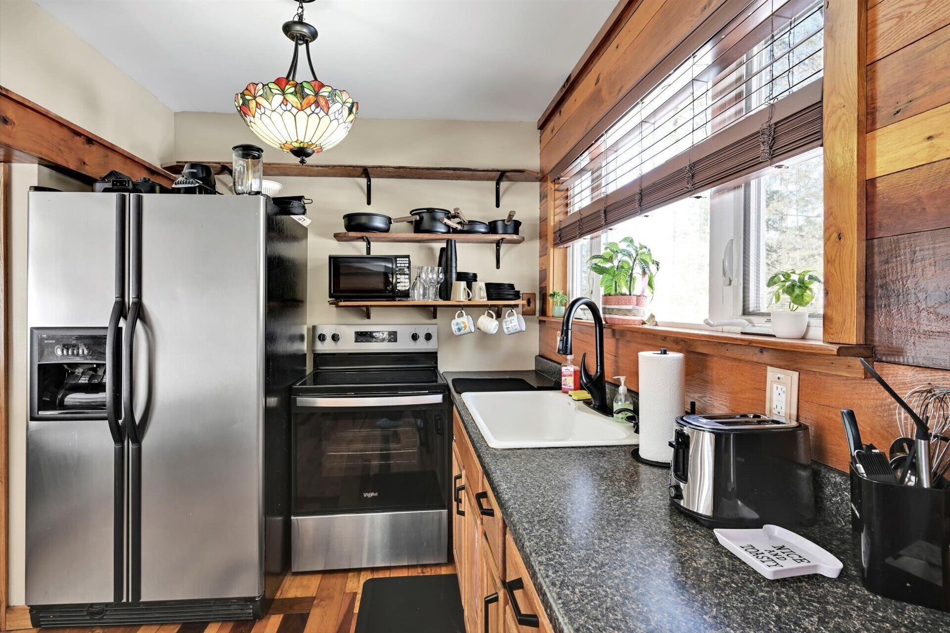 A modern kitchen with stainless steel appliances, wooden accents, and a large window providing natural light.