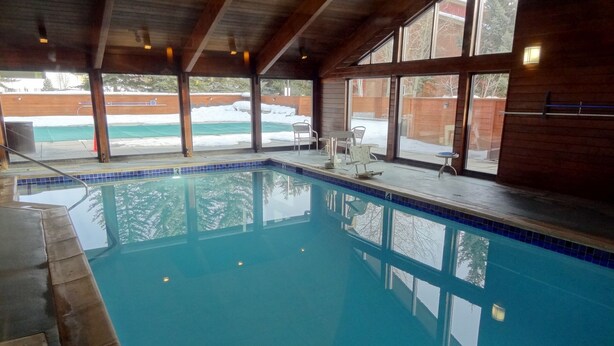 En inomhuspool med kristallklart blått vatten, stora fönster och ett träpanelat tak.