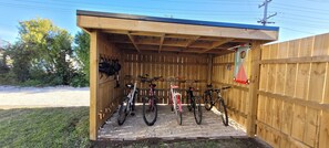 A wooden shed with a roof, containing bicycles and helmets.