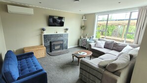 A living room with a fireplace, a sofa, a blue chair, and a television on the wall. - Central Blenheim Character House - Kitchen, Laundry, BBQ, Bikes (Blenheim)