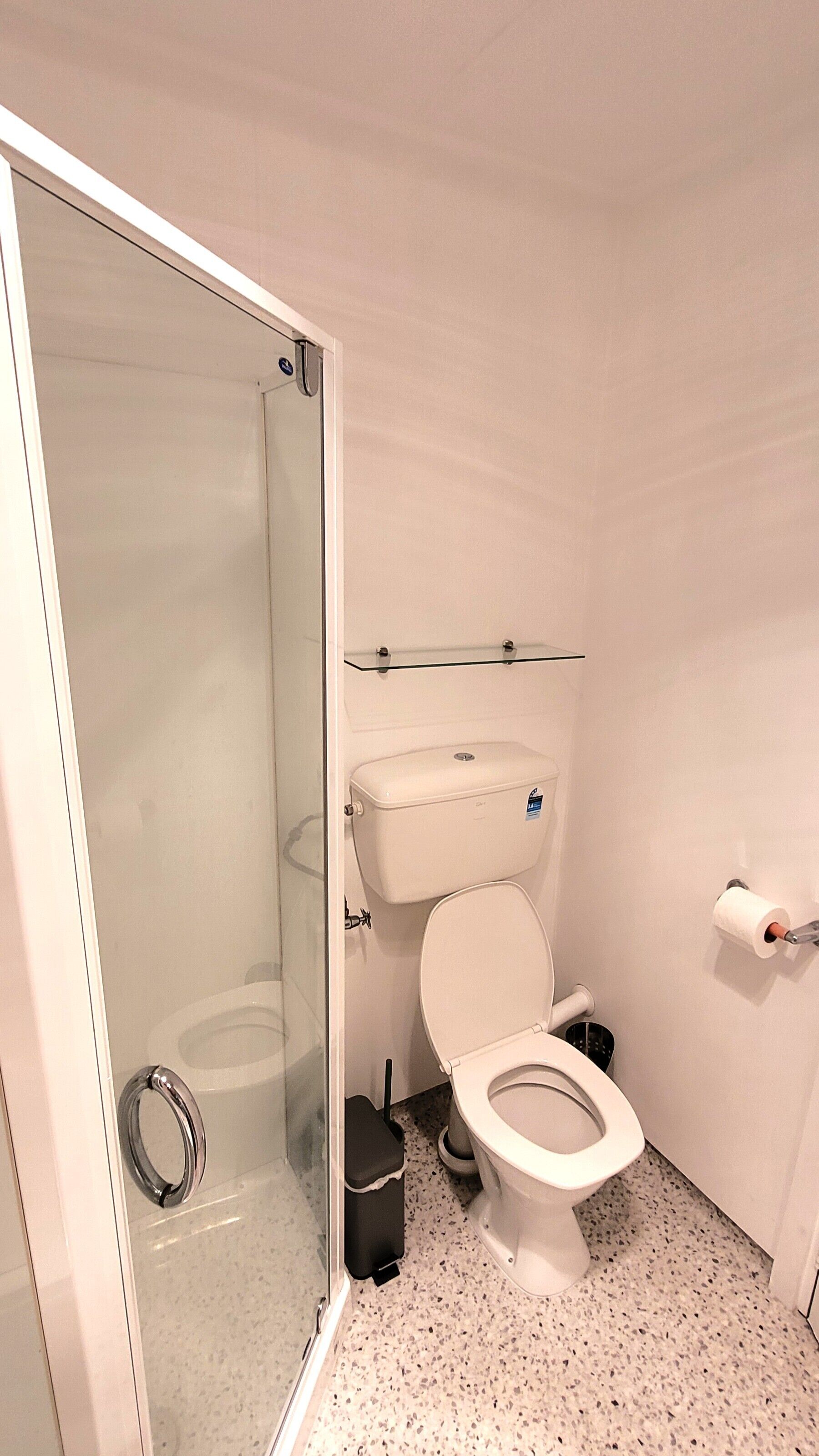 Un baño pequeño y moderno con cabina de ducha de vidrio, inodoro y lavamanos.