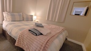 A neatly made bed with pillows and a blanket, a bedside table with a lamp, and a mirror on the wall. - Central Blenheim Character House - Kitchen, Laundry, BBQ, Bikes (Blenheim)
