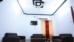 Ein Zimmer mit zwei Sofas, einem Couchtisch, einem Deckenventilator, einem an der Wand montierten Fernseher und einem Fenster mit Vorhängen.