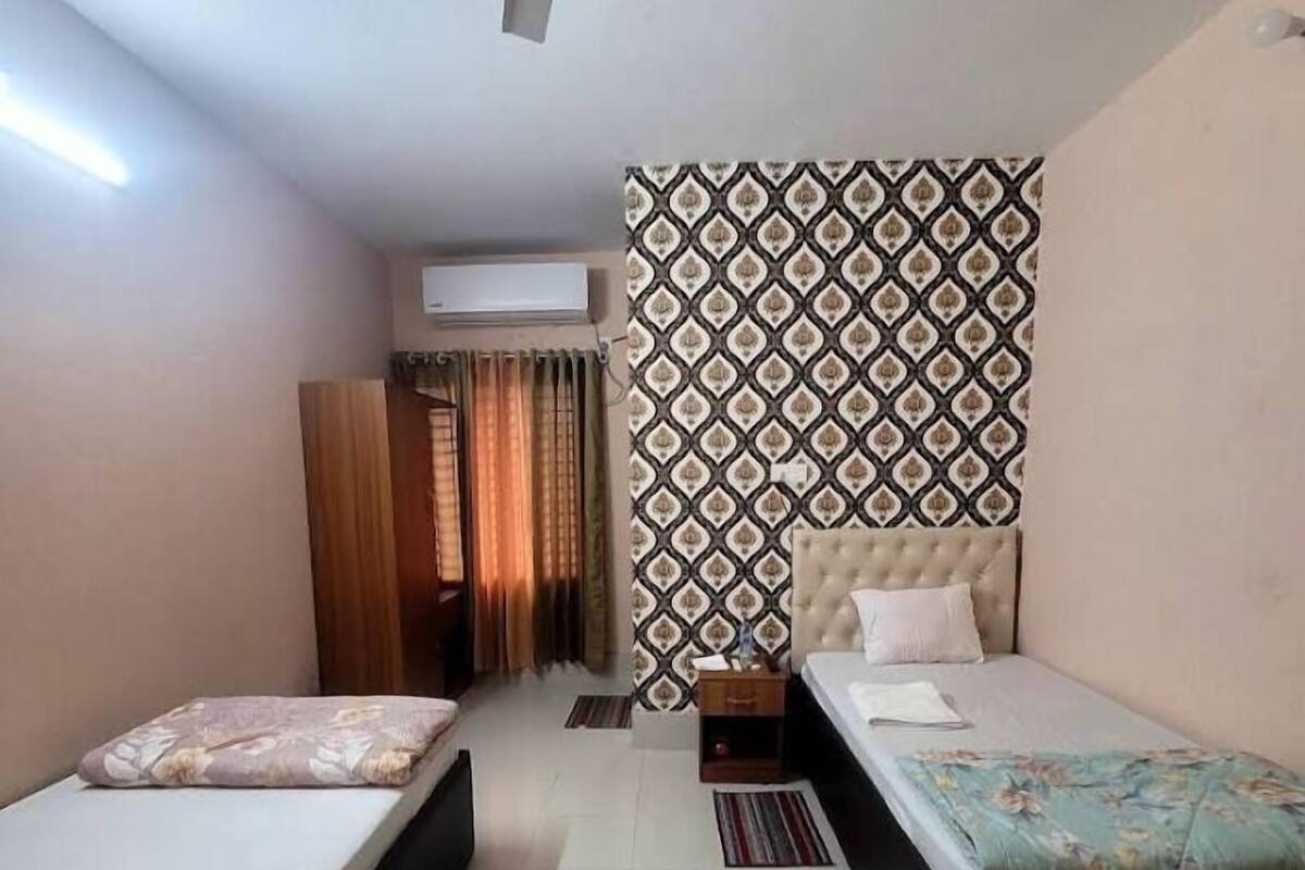 Una habitación con dos camas individuales, ventilador de techo, papel tapiz estampado y una ventana con cortinas.
