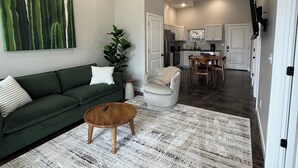 A living room with a green sofa, a coffee table, and a large cactus painting on the wall.
