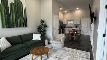 Un salon avec un canapé vert, une table basse et un grand tableau représentant un cactus accroché au mur.