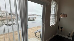 A room with a sliding glass door leading to a balcony overlooking a body of water, a small table, and a potted plant.