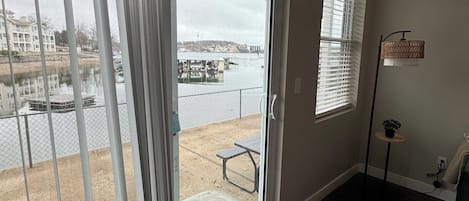 A room with a sliding glass door leading to a balcony overlooking a body of water, a small table, and a potted plant.