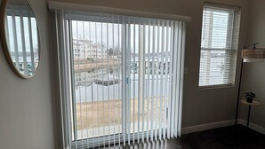 A room with a large sliding glass door, a small window, a round mirror, and a dark floor.