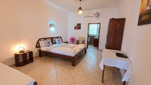 Un dormitorio con cama, mesita de noche y una pequeña mesa con ventilador.