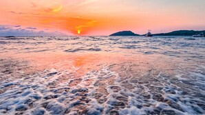 Una playa con olas y una puesta de sol al fondo.