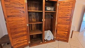 Un armario de madera con varios estantes y una barra para colgar, que contiene una manta doblada y una radio.
