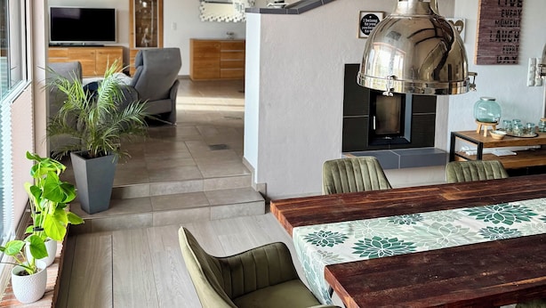 A modern kitchen with a hanging light fixture, a dining area with a wooden table and chairs, and a staircase leading to an upper level.