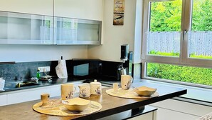 A modern kitchen with a central island, overhead pendant lights, and a view of greenery outside.