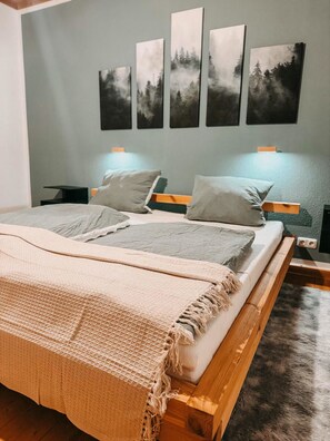 Ein Schlafzimmer mit einem hölzernen Bett, grauer Bettwäsche und vier an der Wand befestigten Gemälden mit Waldmotiven.