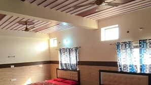 A hotel room with two beds, a ceiling fan, and a large window with curtains. - Sudama Krishna Residency (Mathura)